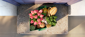 Overhead view of a door stoop with a grocery delivery bag containing flowers, bread, olive oil and produce, where the bag's shape forms Stripe's parallelogram logo.